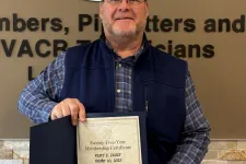 Thumbnail for Man holding a certificate in front of a plumbers and pipefitters union sign and wall with text.