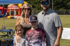 Thumbnail for Family of four posing at outdoor festival with tents, inflatable bounce houses, and sunny weather