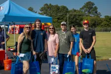Thumbnail for Group of six people smiling outdoors at a community event with blue tents and inflatable play structures.