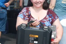Thumbnail for Smiling woman in floral dress holding a black Vault equipment case at an outdoor event.