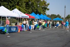Thumbnail for People gather at an outdoor event with tents and booths offering information and goods on a sunny day.
