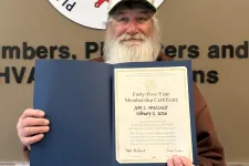 Thumbnail for Bearded man holding a certificate in front of Plumbers and Pipefitters Local Union 72 sign on wall.