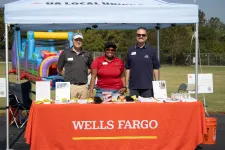 Thumbnail for Three Wells Fargo representatives stand behind an orange table at an outdoor event under a white canopy tent.