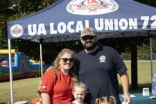 Thumbnail for Family of four standing under UA Local Union 72 tent holding blue Kaiser Permanente bags outdoors.