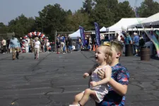 Thumbnail for Boy carrying a smiling toddler girl outdoors with tents and people in the background on a sunny day.