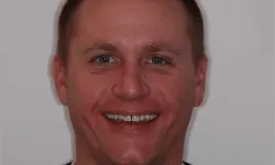 Thumbnail control image for Close-up of a smiling man with short hair and blue eyes against a plain background