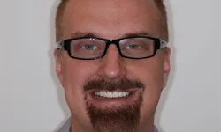 Thumbnail control image for Close-up of a smiling man with glasses, short hair, and a distinctive goatee beard against a plain background