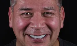 Thumbnail control image for Middle-aged man with dark hair smiling broadly against a black background, wearing a dark gray shirt.