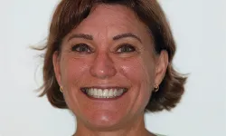 Thumbnail control image for Close-up portrait of a smiling middle-aged woman with short brown hair and gold earrings against a plain background