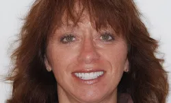 Thumbnail control image for Smiling middle-aged woman with wavy brown hair and green eyes against a plain white background