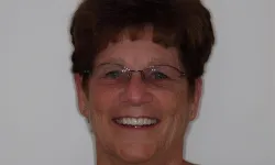 Thumbnail control image for Smiling older woman with short brown hair and glasses against a plain background
