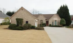 Thumbnail control image for Single-story brick house with well-manicured shrubs, a large driveway, and a dry lawn under a cloudy sky.