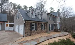 Thumbnail control image for Large two-story suburban house with stone accents, gray siding, white garage doors, and surrounding trees.