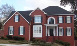 Thumbnail control image for Two-story red brick house with black shutters, white trim, and a black roof surrounded by greenery and lawn.