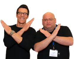 Two men wearing black shirts crossing their arms to form an X gesture, smiling and posing against a white background.