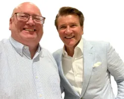 Two smiling men posing for a photo, one in glasses and a striped shirt, the other in a light blue suit jacket.