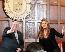 Two speakers seated in front of Harvard Club of Boston emblem during a discussion or event.