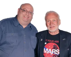 Two men smiling, one in glasses and blue shirt, the other wearing Mars graphic t-shirt and black jacket