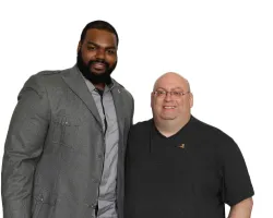 Two men posing together, one in gray suit and the other in black shirt, smiling against white background