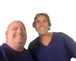 Two men wearing blue shirts smiling in front of a plain white background