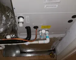 Indoor HVAC unit with connected copper and PVC pipes for heating and cooling system operation.