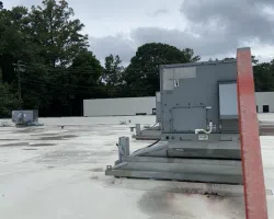 Commercial building rooftop with HVAC units mounted on a flat white roof under cloudy sky.
