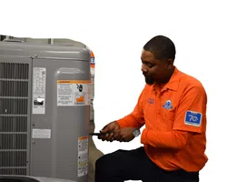 Technician in orange shirt repairing or maintaining a gray HVAC unit with a screwdriver indoors.