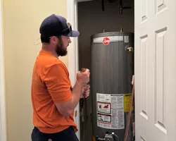 Technician inspecting or repairing a residential water heater inside a utility closet with an open white door.