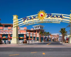 Entrance sign of Pier Park with palm trees and colorful buildings under clear blue sky in Panama City Beach.