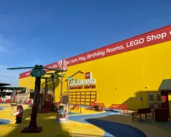 Bright yellow LEGOLAND Discovery Center building with colorful playground and clear blue sky overhead.