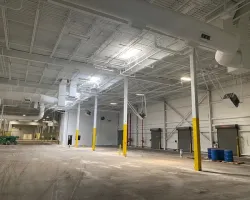 Spacious empty warehouse interior with high ceilings, yellow safety poles, and industrial lighting fixtures.