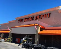 The Home Depot store exterior with orange awnings, American flags, and grills displayed outside on a sunny day.