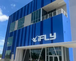 Modern blue building with iFLY logo and large glass windows under a clear sky.