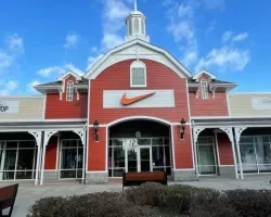 Exterior of a red and beige Nike store with a large orange swoosh logo under a blue sky