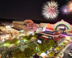 Night scene of a vibrant shopping plaza with crowds, Regal Cinemas lit up and fireworks in the sky