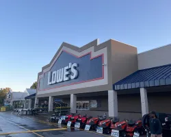 Exterior of Lowe's home improvement store with riding lawn mowers displayed outside on a clear day.