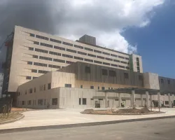 Modern multi-story hospital building under construction with clear sky and surrounding paved areas