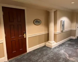 Hotel hallway with a wooden door labeled Charter Room, beige walls, white column, and patterned carpet.