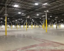 Large empty warehouse interior with yellow support columns and high ceiling lights evenly spaced.