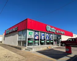 O'Reilly Auto Parts store with red exterior, promotional posters, a customer, and a parked red vehicle.