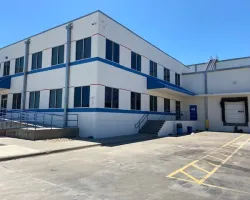 Modern industrial warehouse exterior with loading dock and accessibility ramp under clear blue sky.