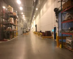 Spacious industrial warehouse aisle with shelves stocked with boxes and equipment under bright overhead lighting