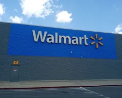 Exterior of a Walmart store with large blue signage and gray walls under a partly cloudy sky.