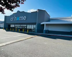 At Home store exterior with clear signage and empty parking lot under blue sky and tree branches.