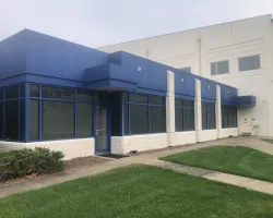 Modern commercial building with blue and white facade surrounded by green lawn and sidewalk.