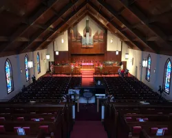 Interior view of a church with wooden pews, stained glass windows, an organ, and a high vaulted ceiling.