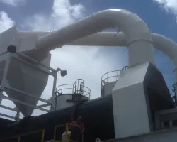 Large industrial machinery with white ducts and cylindrical tanks under a blue sky with clouds.