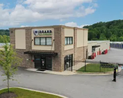 Modern self-storage facility with brick office, gated access, and rows of storage units under a blue sky.