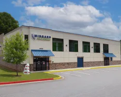 Midgard Self Storage office building with blue awnings and ample parking under a blue sky with clouds.