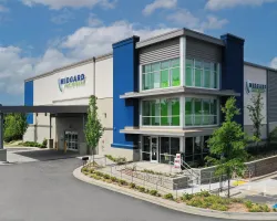 Modern commercial building with blue accents and large glass windows under a partly cloudy sky.